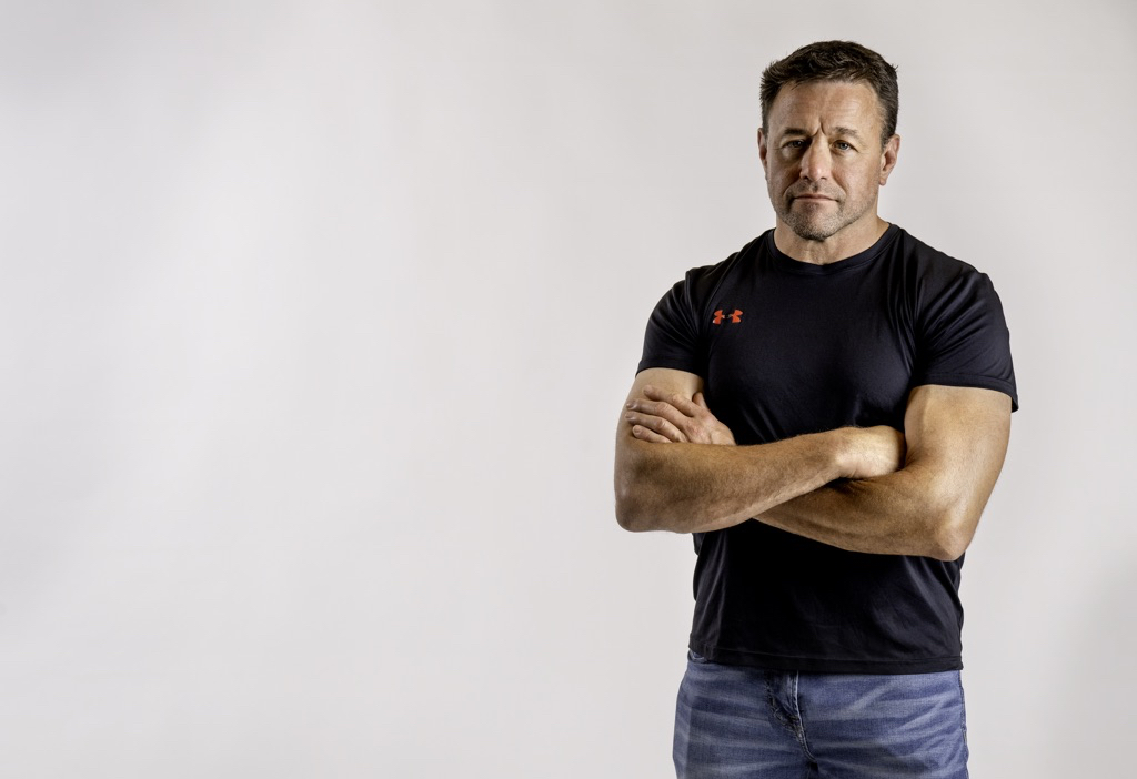 Alan Baker standing with arms crossed in a black shirt