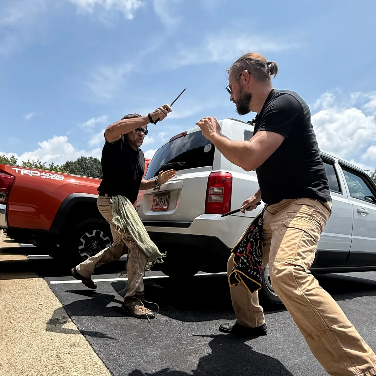 Alan Baker and a training partner practicing defensive tactics beside a vehicle