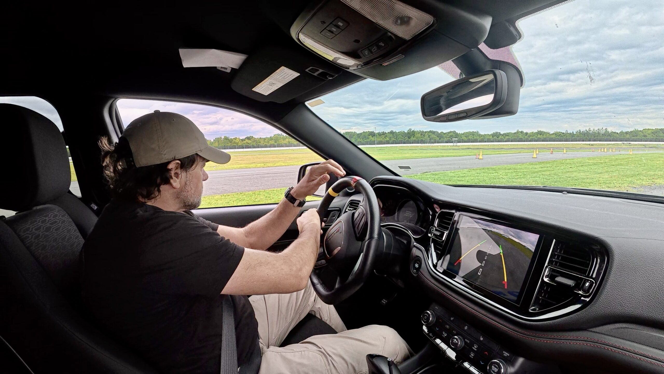 Alan Baker taking a driving course at Vehicle Dynamics Institute, seated at the wheel on a cone-marked training course.