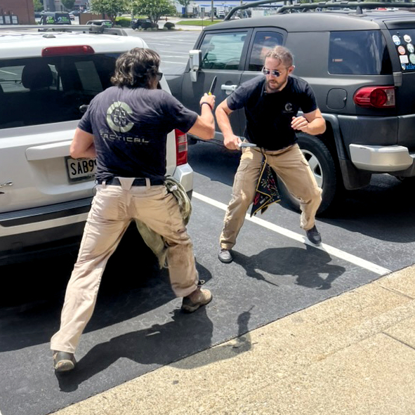 Two training partners facing each other in the space between parked vehicles.